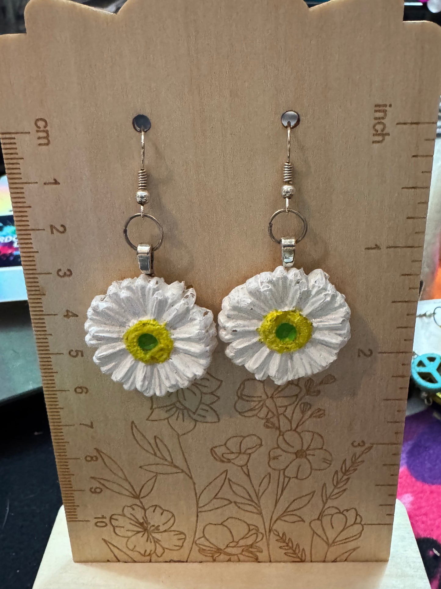 Flower-shaped earrings on a wooden stand with measurements.