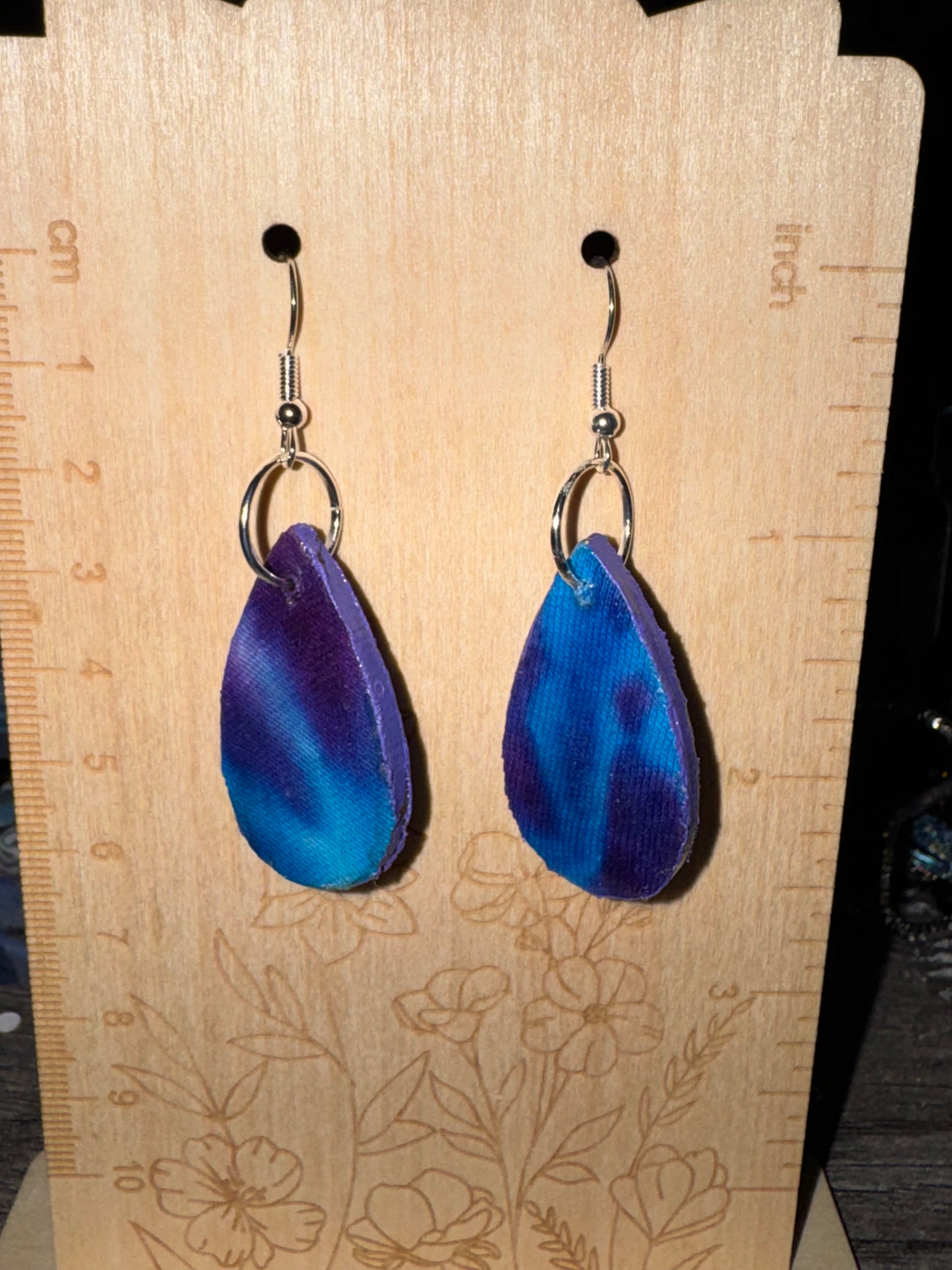 Blue earrings on a wooden surface with a ruler for scale