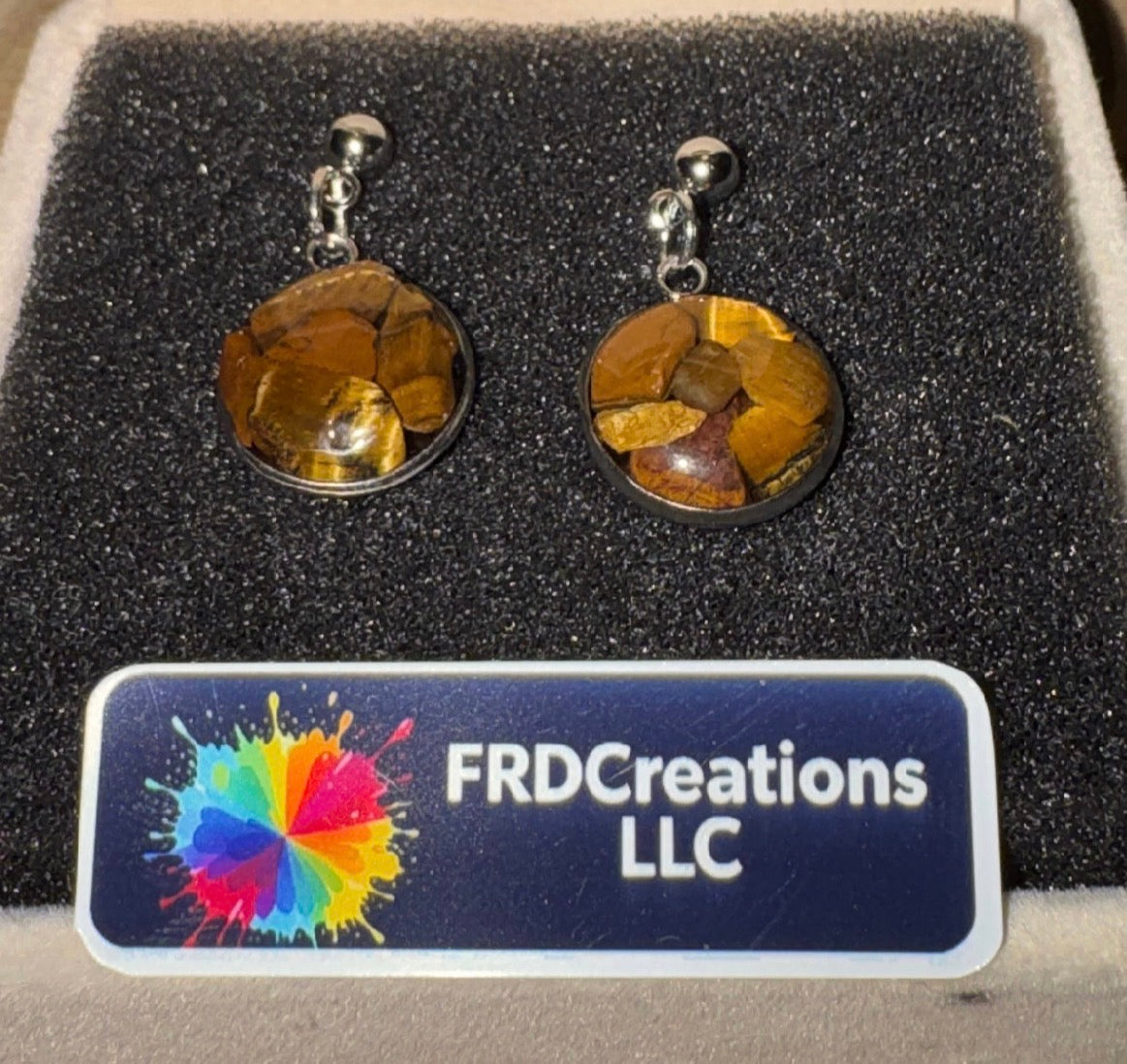 Pair of tiger eye stone earrings on a black cushion with FRDCreations LLC label.