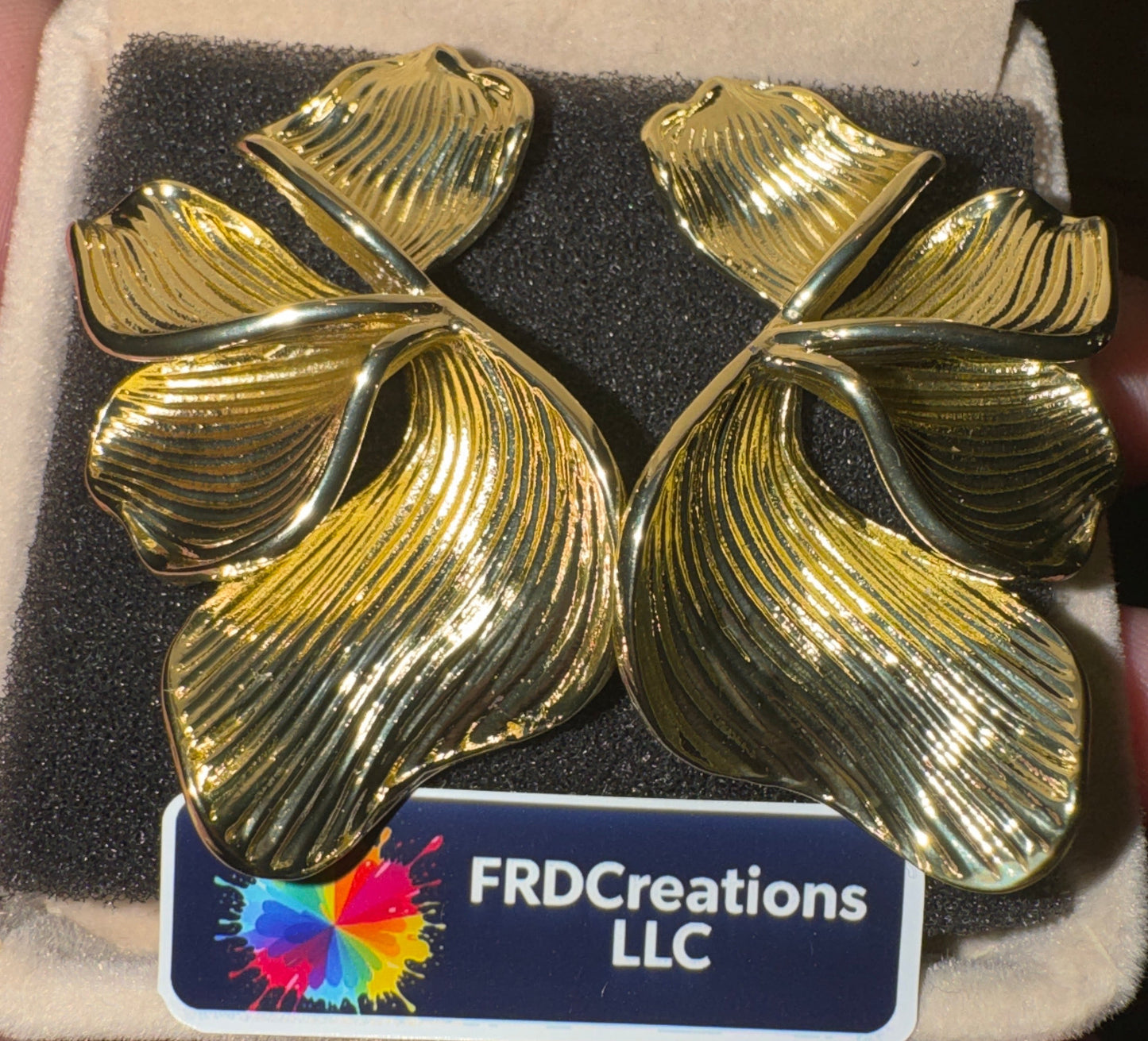 Gold leaf-shaped earrings in a box with FRD Creations LLC label.