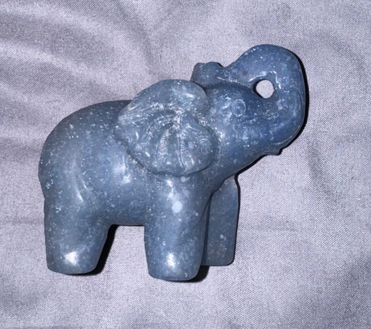 A small carved elephant figurine made of speckled slate blue stone, resting on a textured gray fabric background.