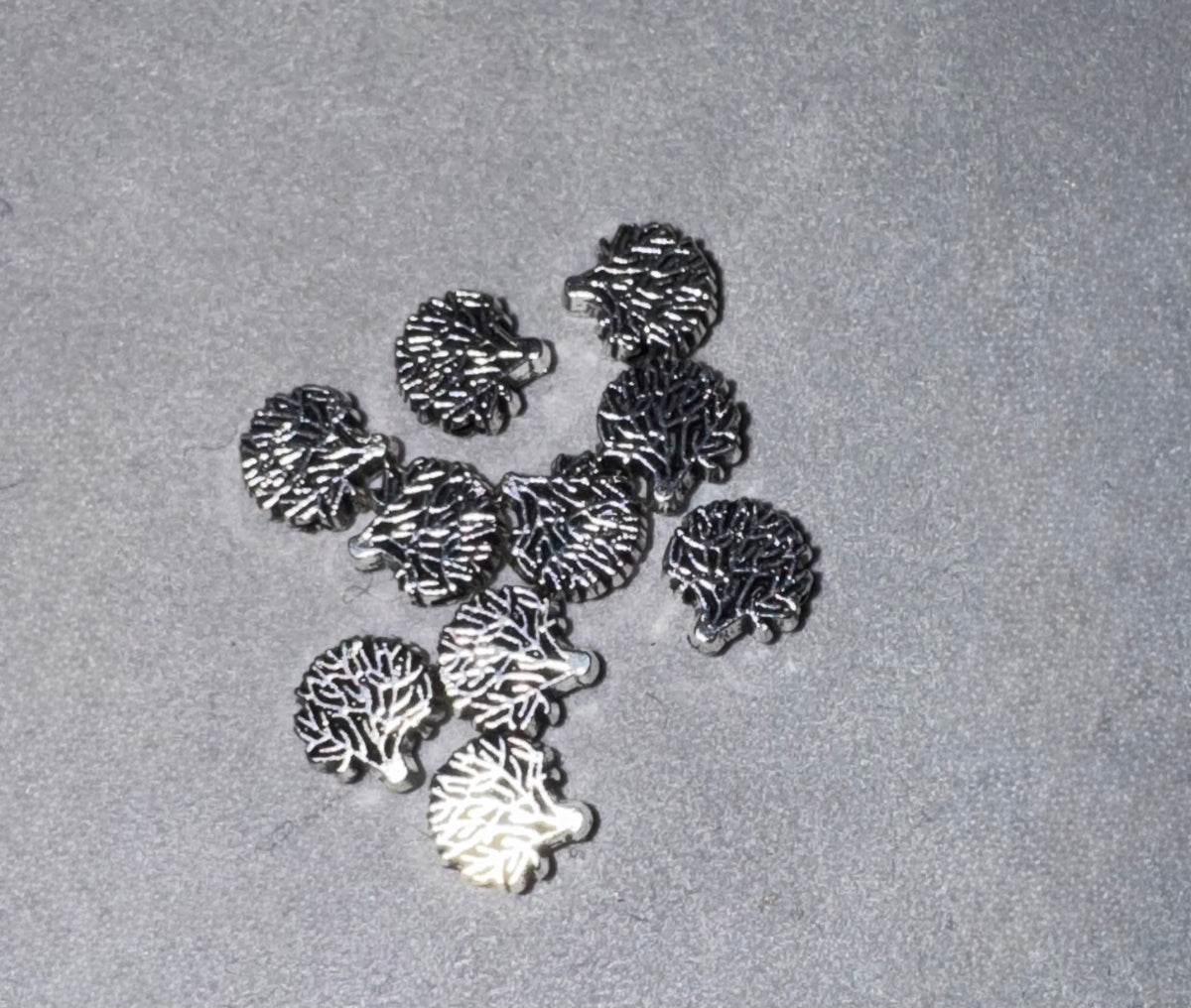 A group of small metallic jewelry charms shaped like hedgehogs, displayed on a textured gray surface.