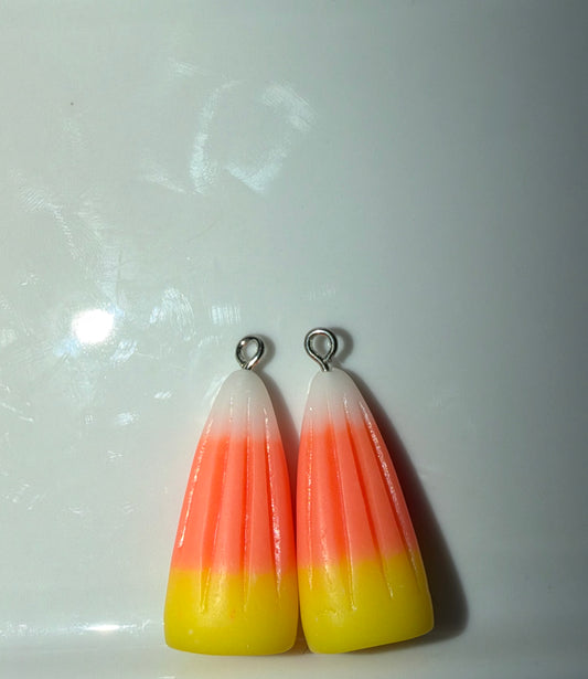 Two candy corn-shaped jewelry charms with silver jump rings, featuring a three-stripe gradient of white, orange, and yellow, set against a plain light background.