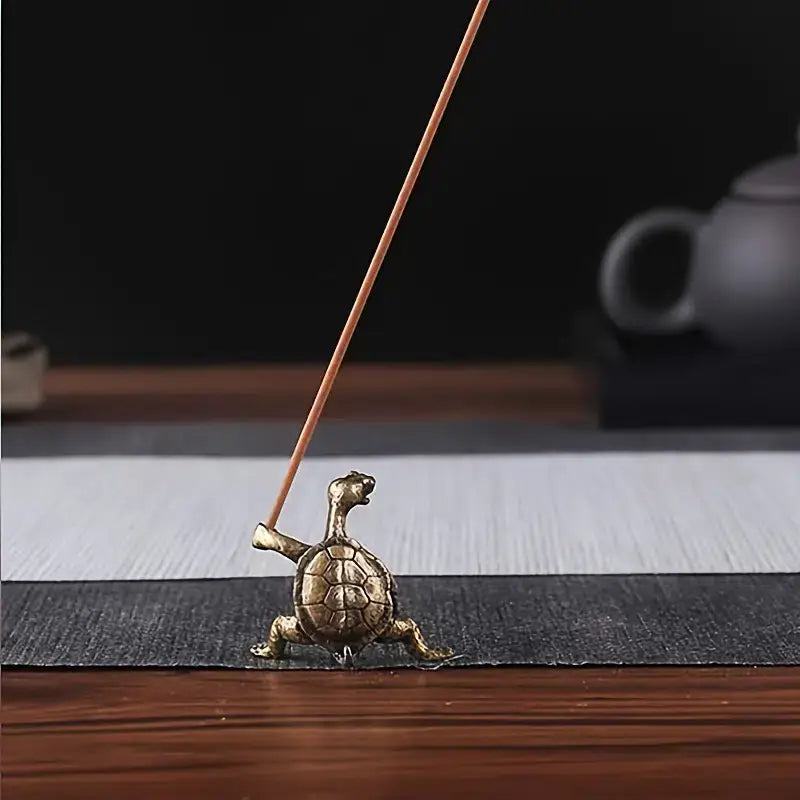 Bronze turtle incense holder with a lit incense stick on a wooden surface.
