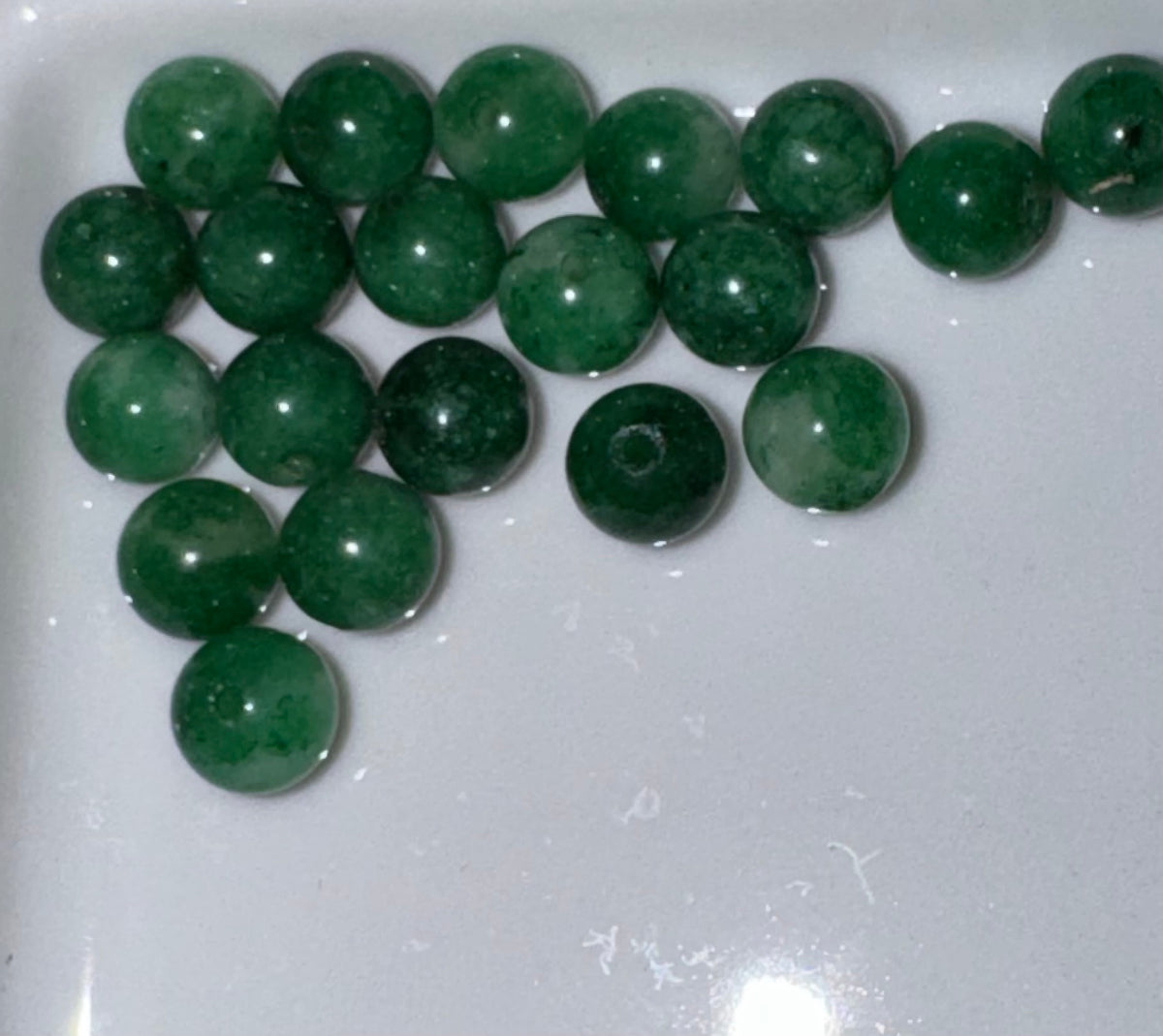 A group of polished round green beads with visible natural inclusions, arranged on a white surface.