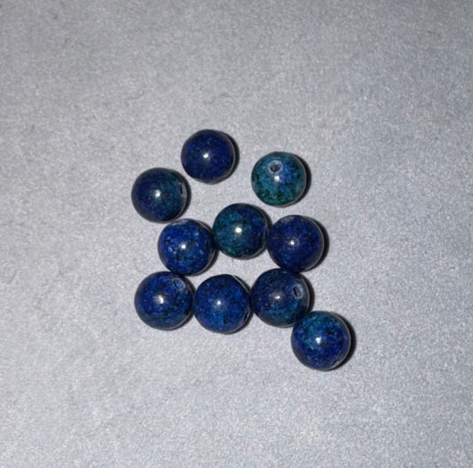 Nine round blue lapis lazuli stone beads with dark flecks, arranged in a small cluster on a textured light gray background.