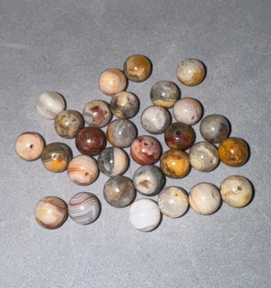 A group of round stone beads with natural marbled patterns in earthy tones of brown, beige, gray, and white, arranged on a textured gray background.