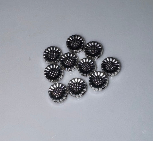 A group of small round silver-toned metal beads with a textured, scalloped edge and a dotted pattern on top, arranged on a plain light gray background.
