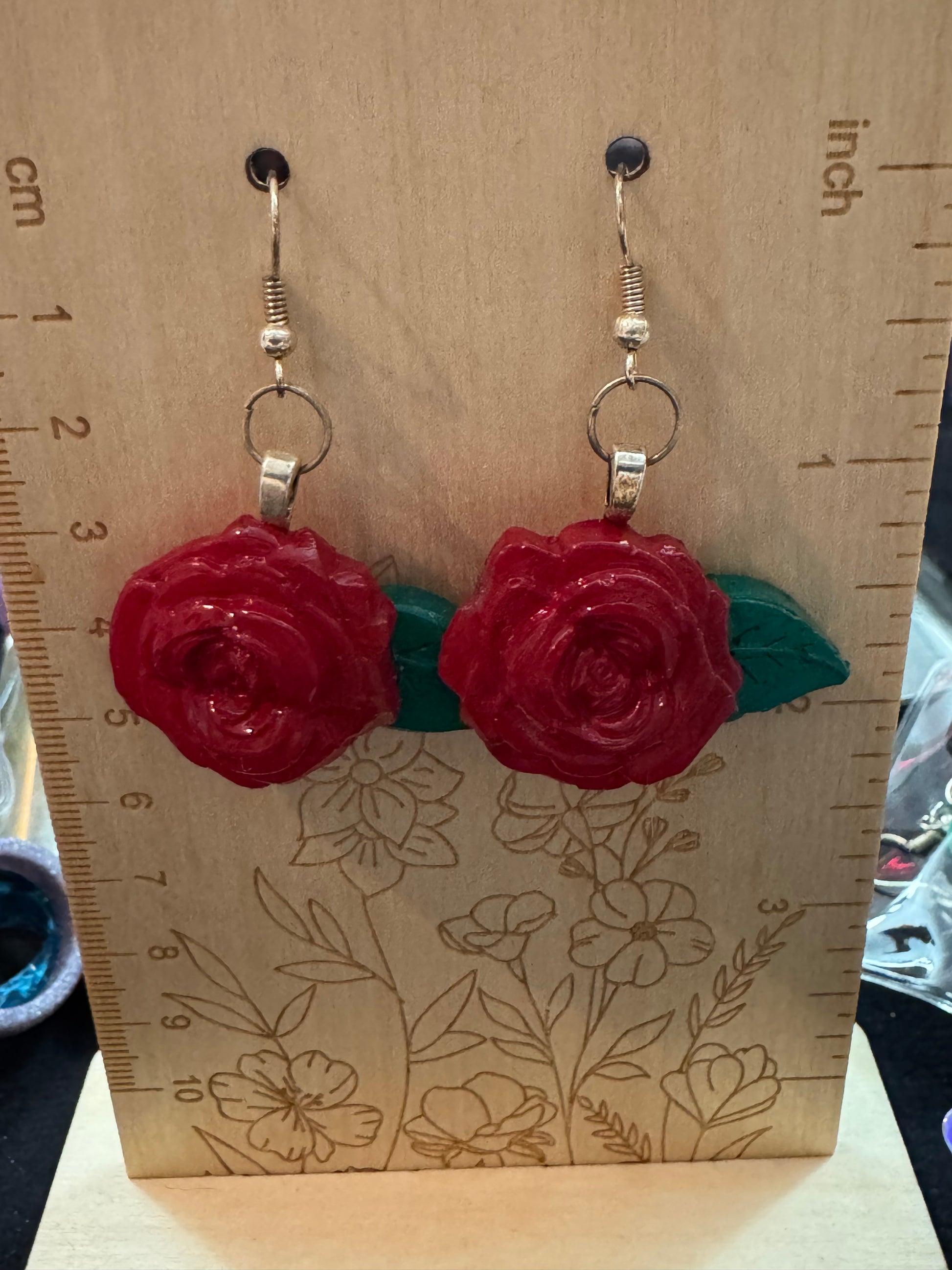 Red rose-shaped earrings on a wooden board with floral patterns and measurements.