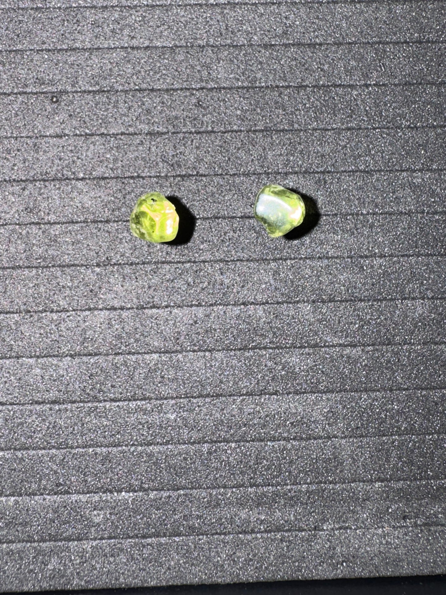Two green earrings on a textured gray surface
