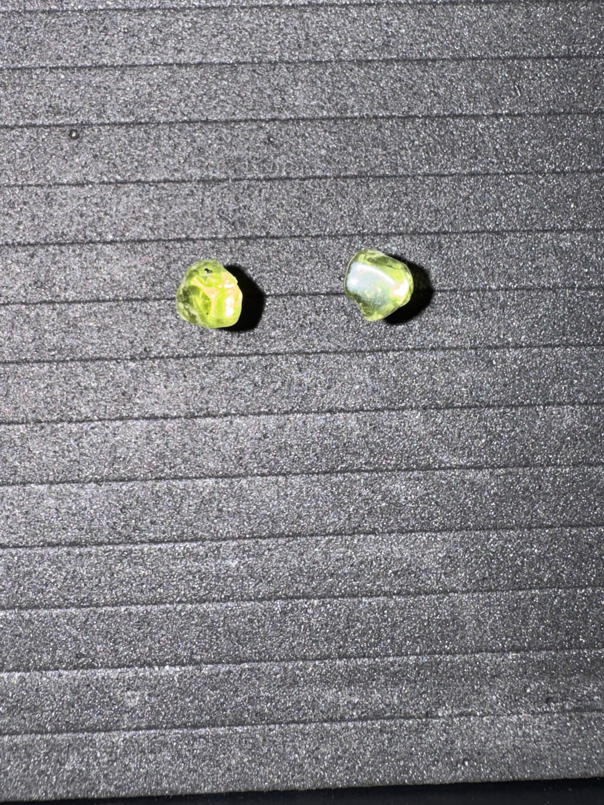 Two green earrings on a textured gray surface
