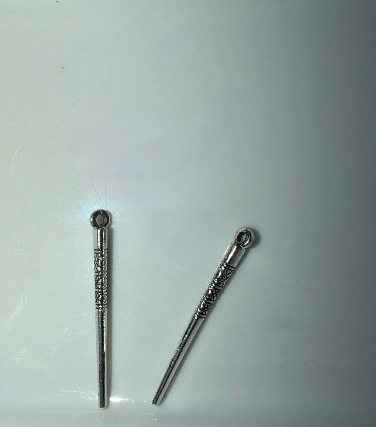 Two silver-toned metal charms with decorative engravings and loop tops, displayed on a plain light background.