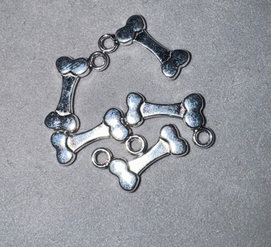 A set of metallic silver bone-shaped charms with small circular loops, arranged on a textured gray background.