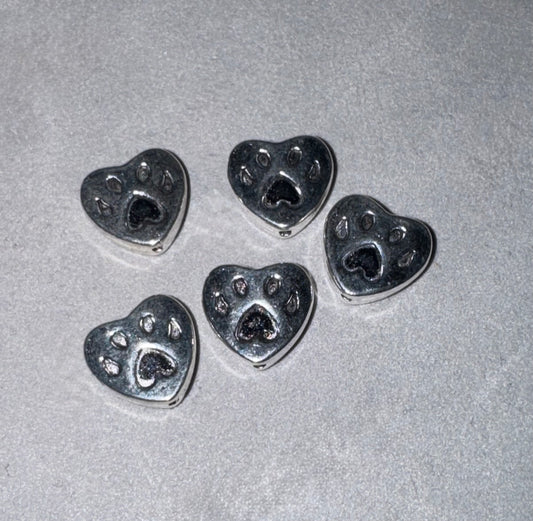 Five silver heart-shaped charms with paw print details, arranged on a textured light gray background.