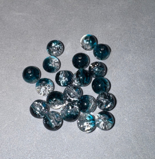 A group of round, dark teal glass beads with white glitter swirls, arranged on a textured gray background.