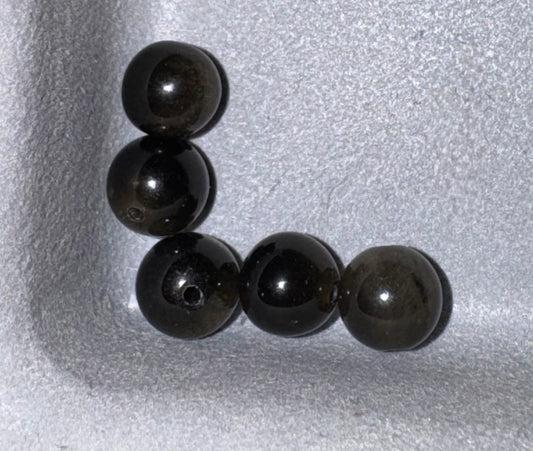 Five dark gray to black polished round beads arranged in a U-shape on a textured light gray foam background.