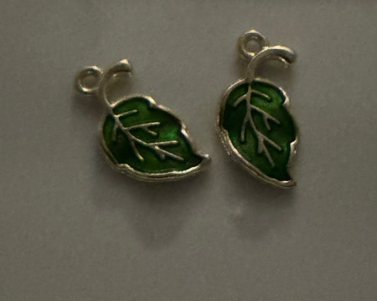 Two small silver leaf-shaped charms with green enamel fill, shown on a plain gray surface.