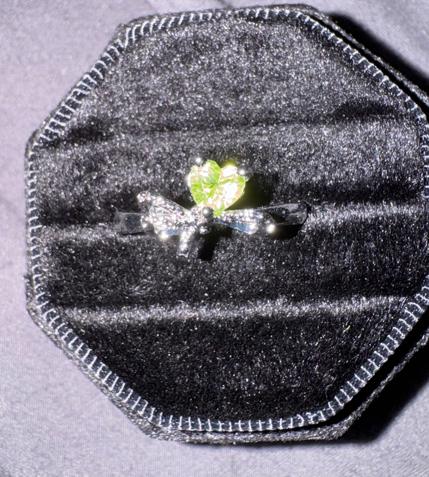 Silver ring with a green gemstone in a black velvet ring box on a gray background