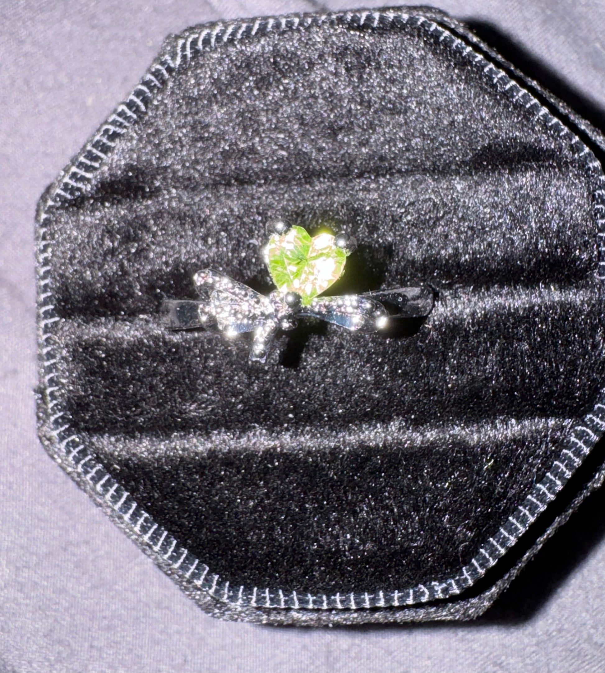 Silver ring with a green gemstone in a black velvet ring box on a gray background