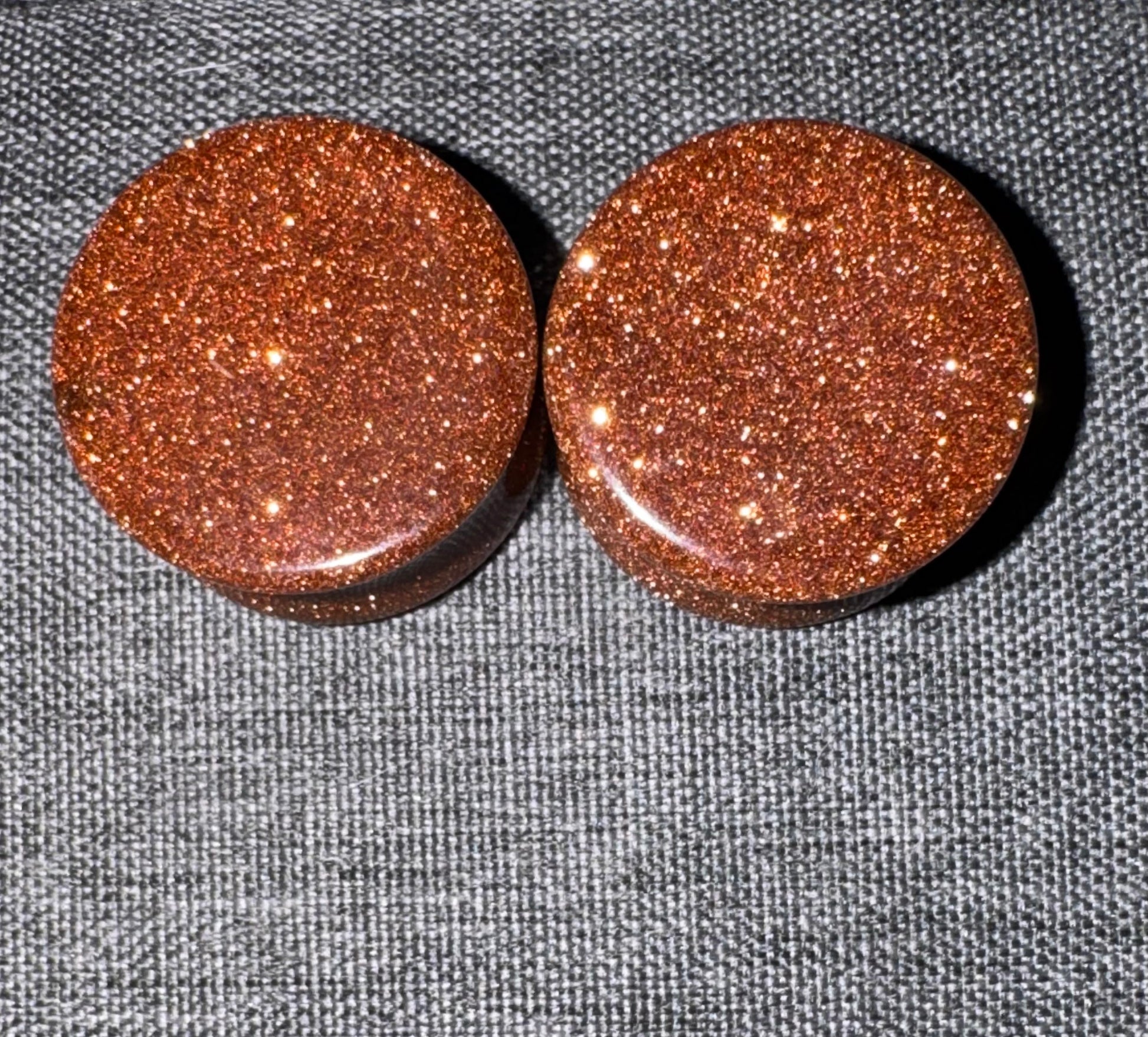 Two round, brown glittery ear gauges on a gray textured background