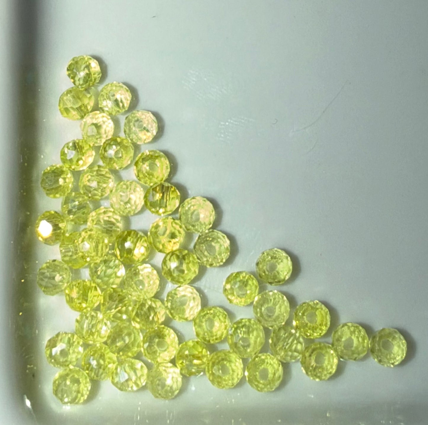 A group of small, round, faceted yellow-green beads clustered in the lower-left corner of a light-colored surface.
