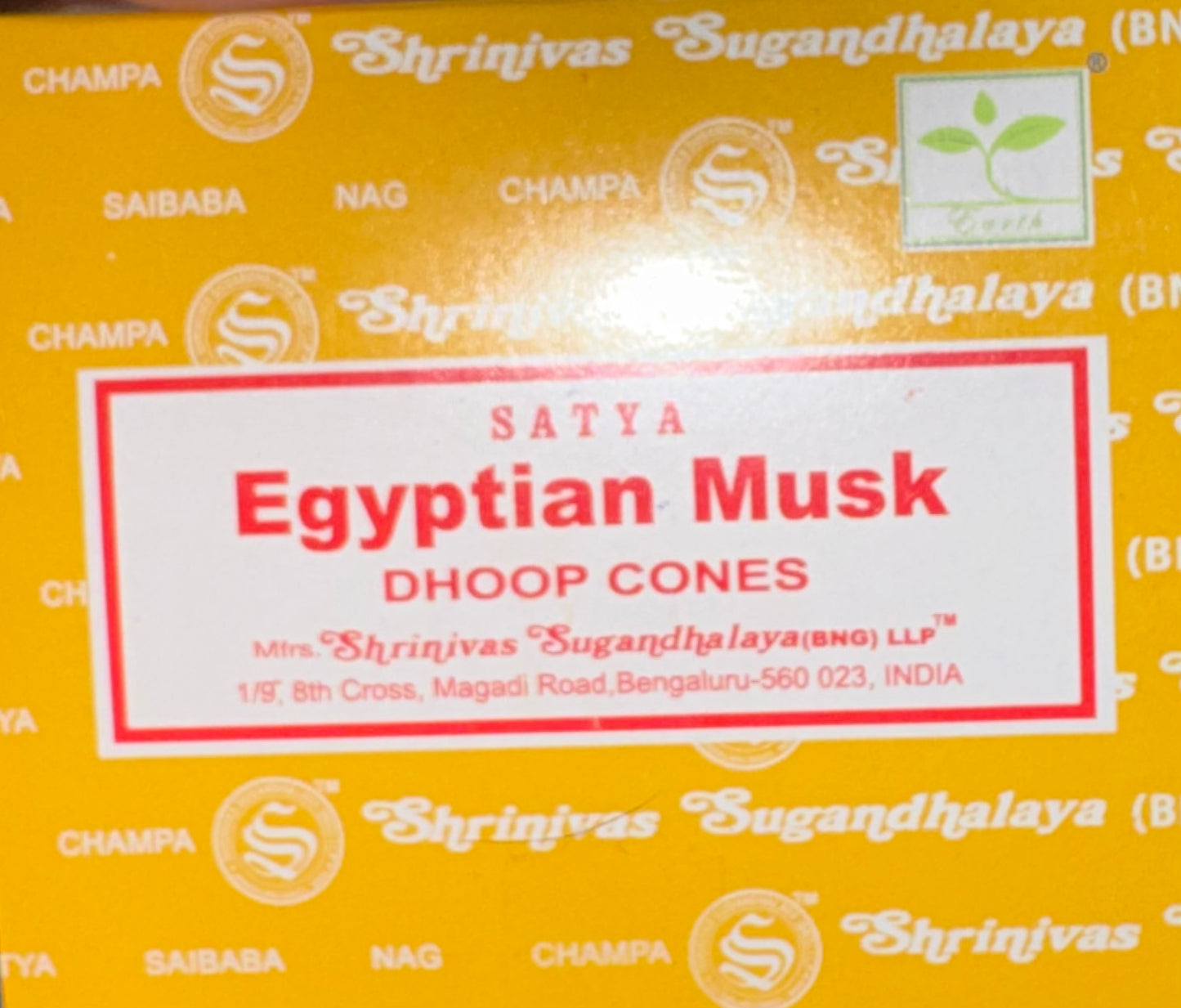 A close-up of a yellow box of Satya Egyptian Musk Dhoop Cones, featuring a white label with red text and a red border. The box has a repeating pattern of other product names like Champa, Saibaba, and Nag in white, along with the Shrinivas Sugandhalaya brand logo.