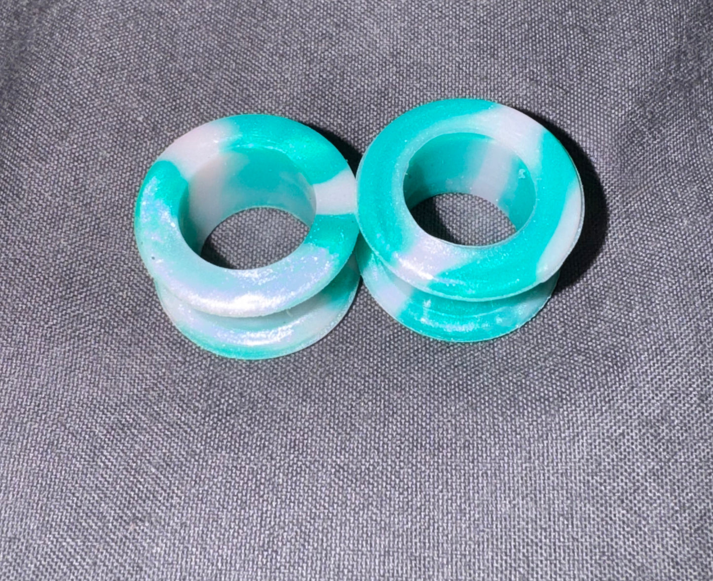 Two round turquoise and white marbled plug earrings on a textured gray fabric background.