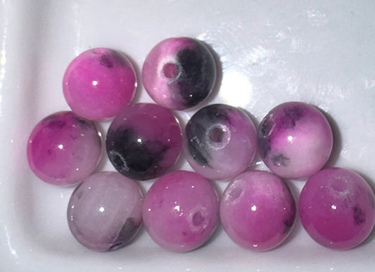 Ten round pink and purple marbled gemstone beads with central holes, arranged on a white ceramic dish.