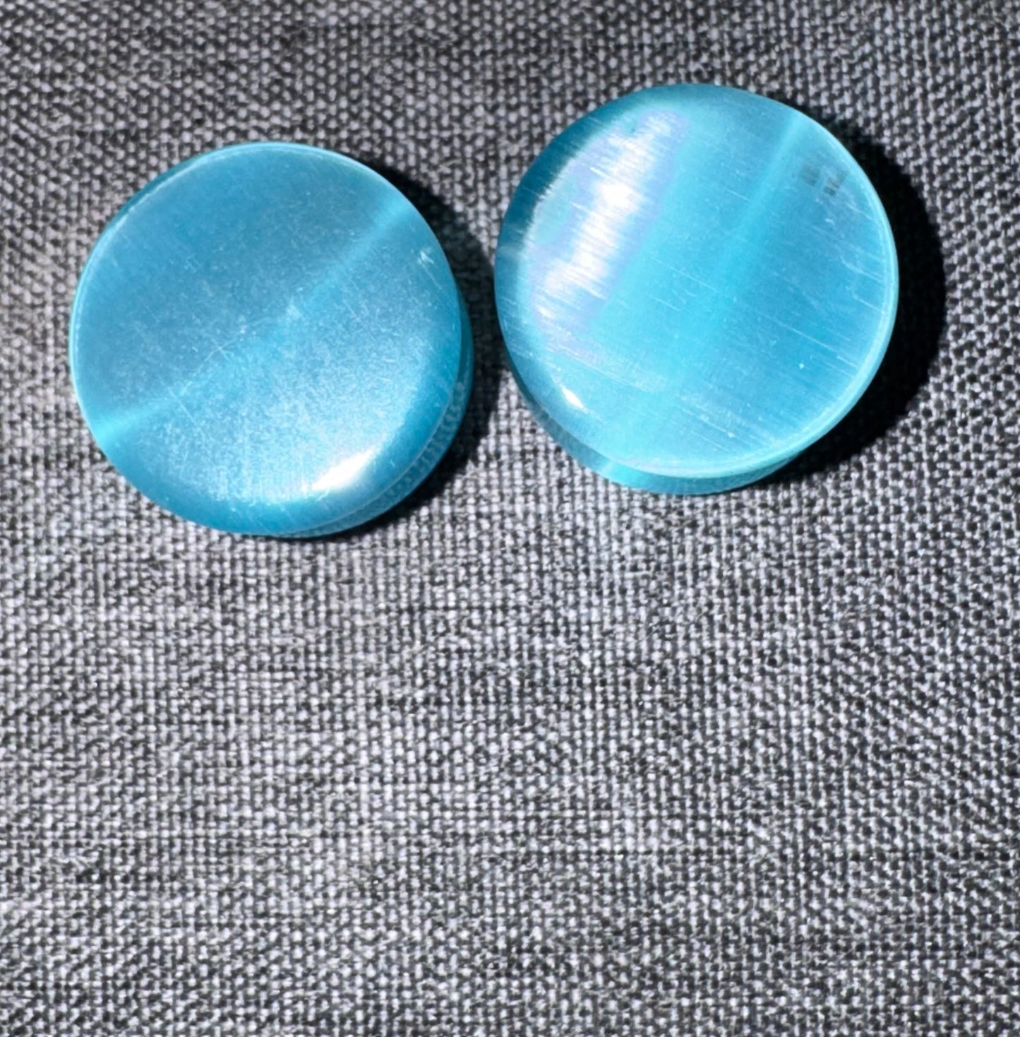 Two blue cat's eye ear gauges on a textured gray surface