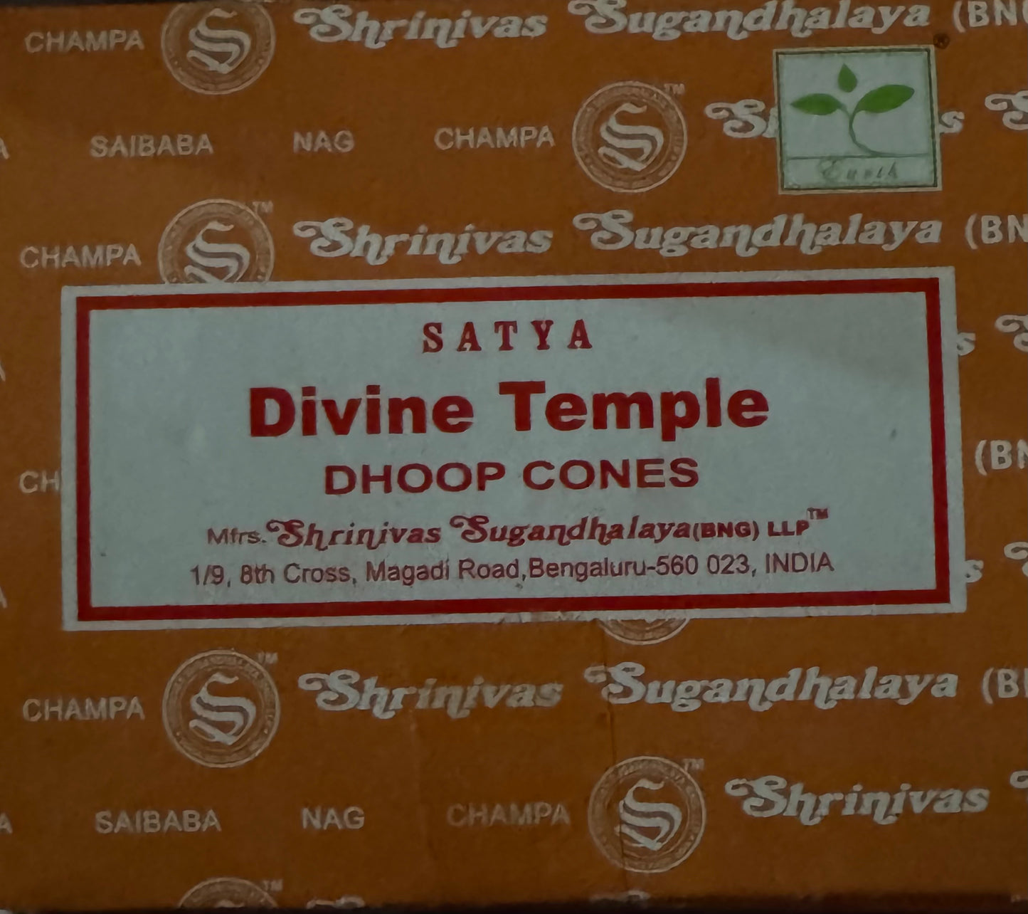 A box of Shrinivas Sugandhalaya Divine Temple Satya Dhoop Cones incense sticks, featuring a white label with red text on an orange-brown patterned background.