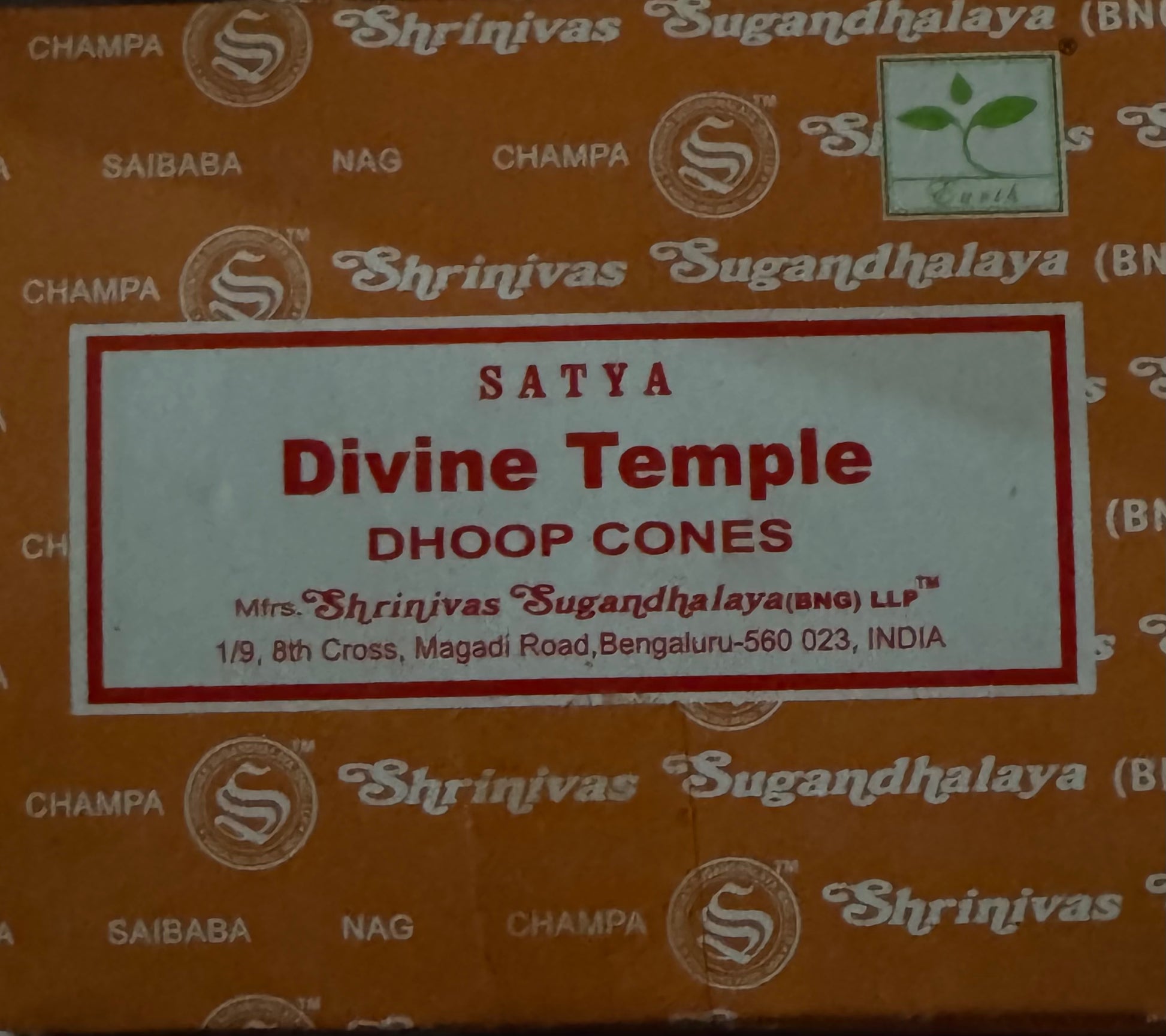 A box of Shrinivas Sugandhalaya Divine Temple Satya Dhoop Cones incense sticks, featuring a white label with red text on an orange-brown patterned background.