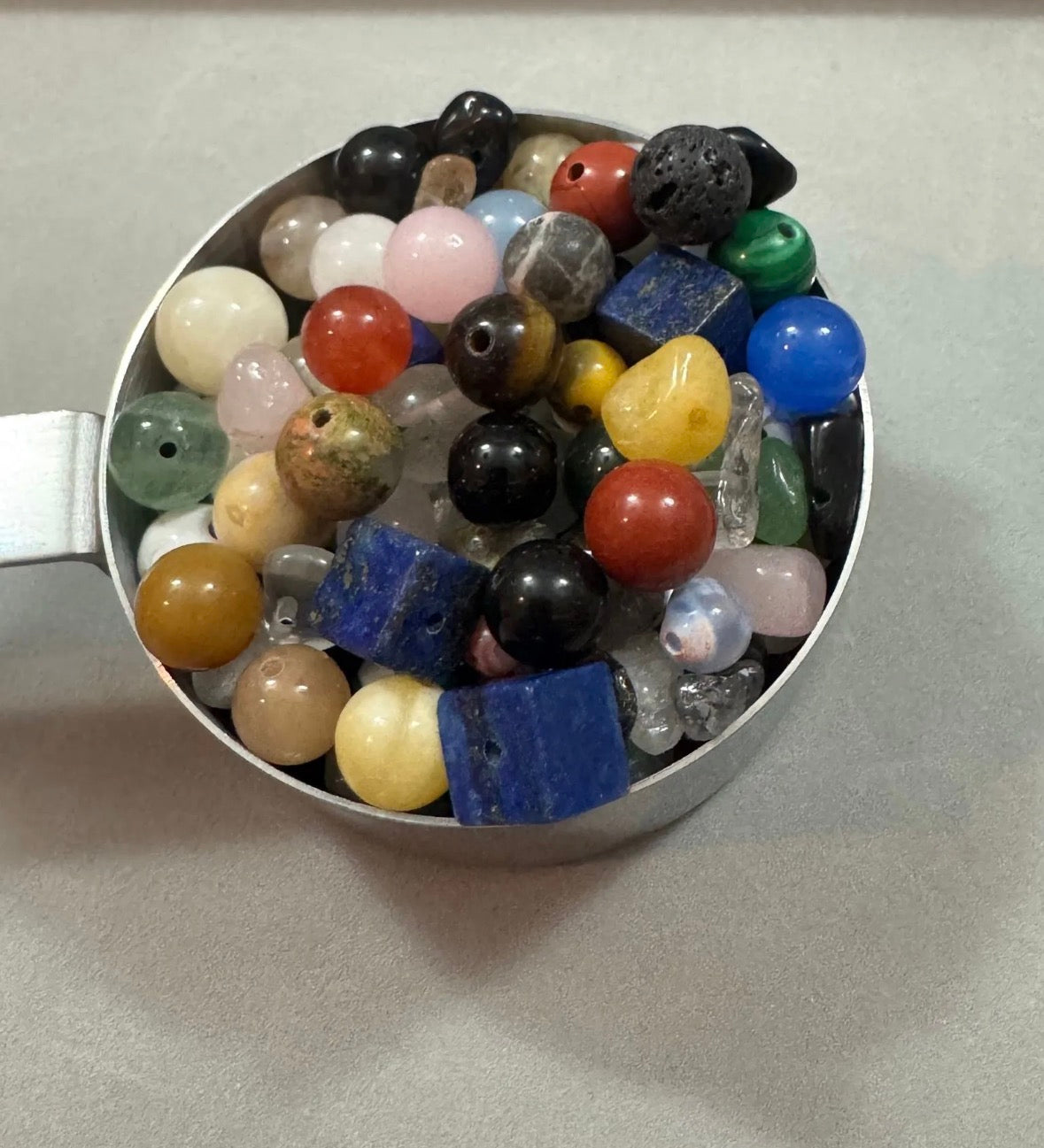 Assorted colorful beads in a metal cup on a light gray background