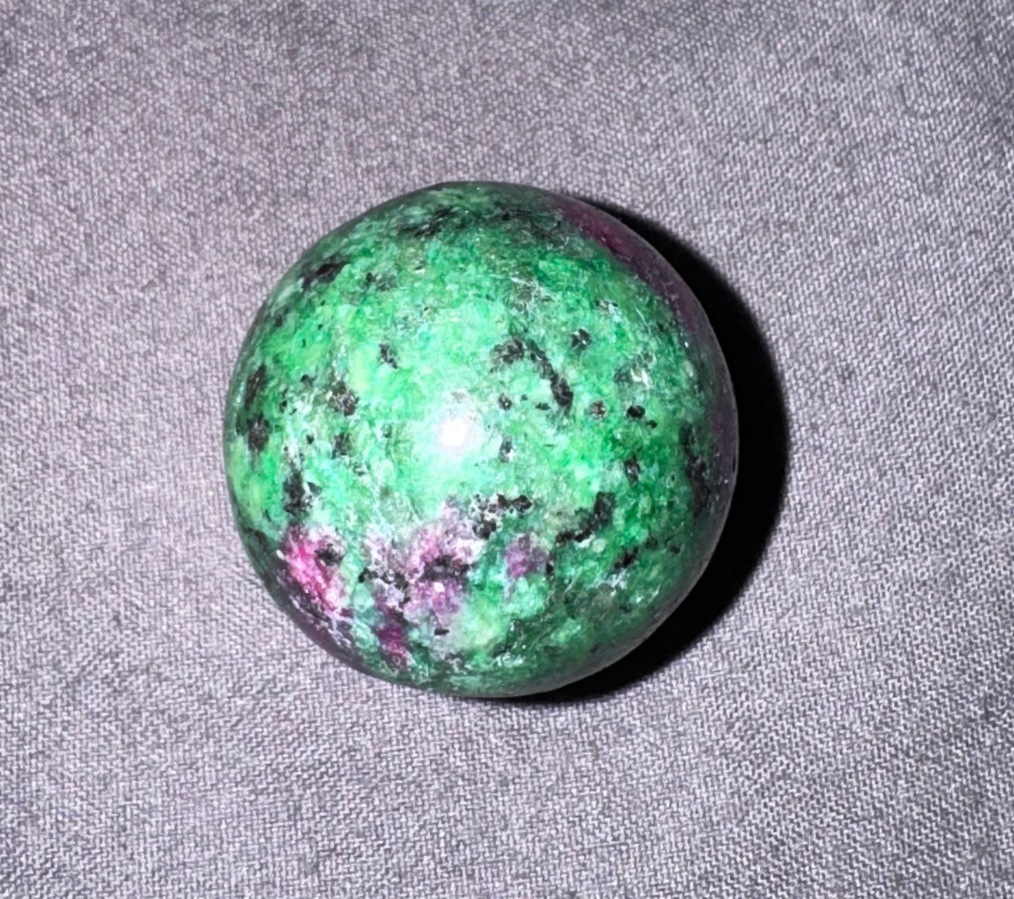 Green stone with purple and black specks on a gray fabric background