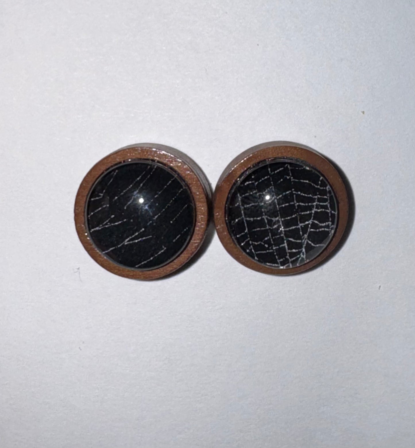 Two round black stone cabochons with natural white veining, set in a warm brown wooden frame, displayed on a light gray background.