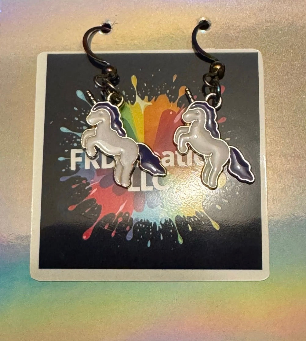 Unicorn-shaped earrings on a card with colorful splashes and text.