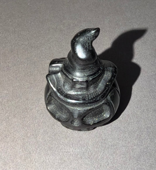 A small black carved figurine of a wizard wearing a pointed hat, photographed on a neutral gray background with a sharp shadow cast to the right.