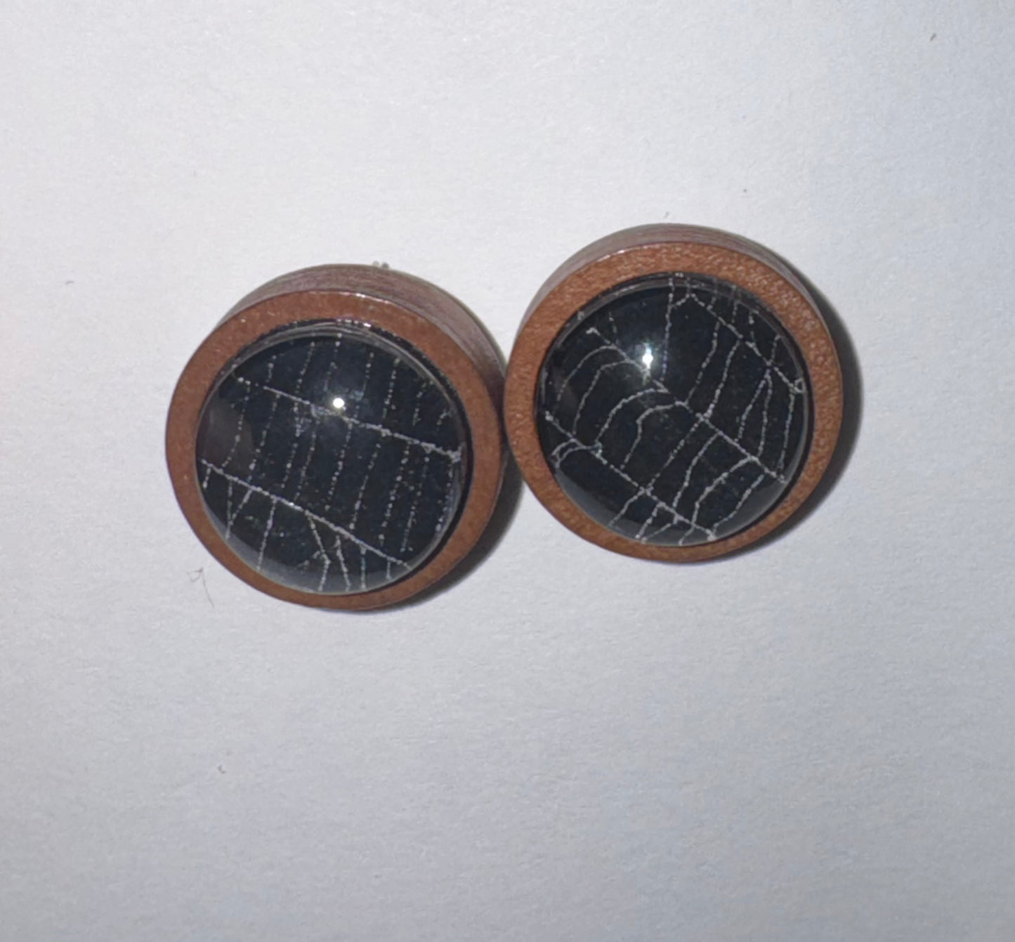 A pair of round wooden stud earrings with dark, cracked stone centers, displayed on a plain light background.