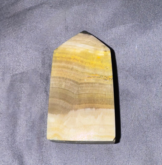 A polished natural stone or mineral block with layered beige, yellow, and brown bands, photographed on a textured gray fabric background.