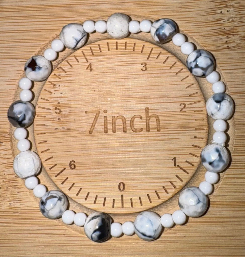 Beaded bracelet with gray and white stones on a wooden measuring tool labeled '7 inch'.