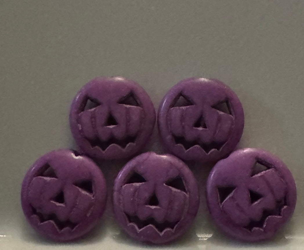 Five round purple jack-o'-lantern face beads arranged in two rows on a plain gray background.