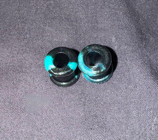 Two small black cylindrical plugs with bright turquoise blue painted accents, placed on a textured gray fabric background.
