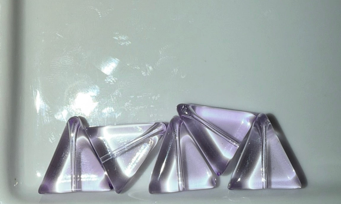 Four triangular lavender-purple gemstone cabochons arranged on a light gray reflective surface.