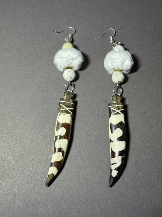 A pair of handmade dangle earrings featuring brown and white cowhide horn blades with white bead details and fluffy white faux fur, displayed on a neutral gray background.