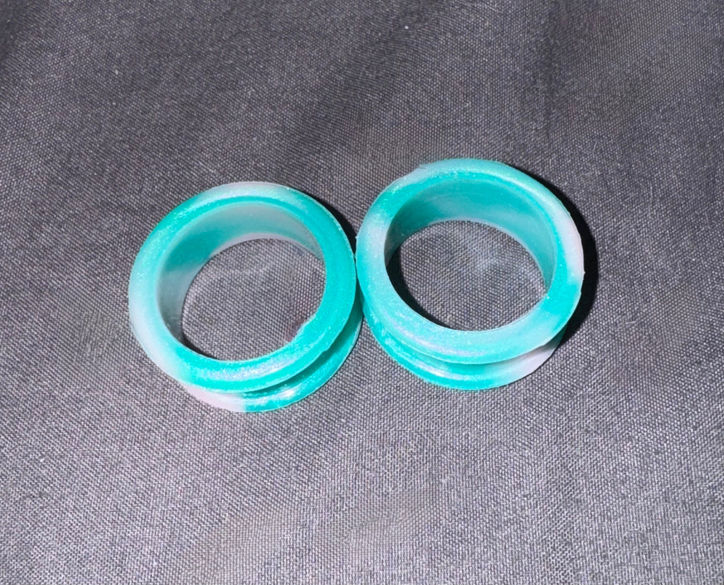 Two translucent aqua blue silicone rings with white inner lining, displayed on a dark gray textured fabric background.