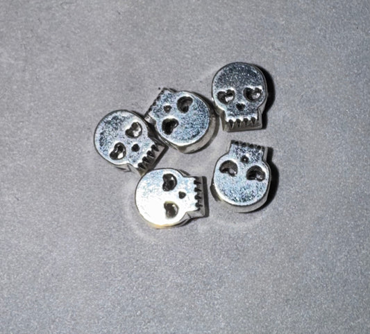 Five small silver skull-shaped beads or charms arranged on a textured gray surface.