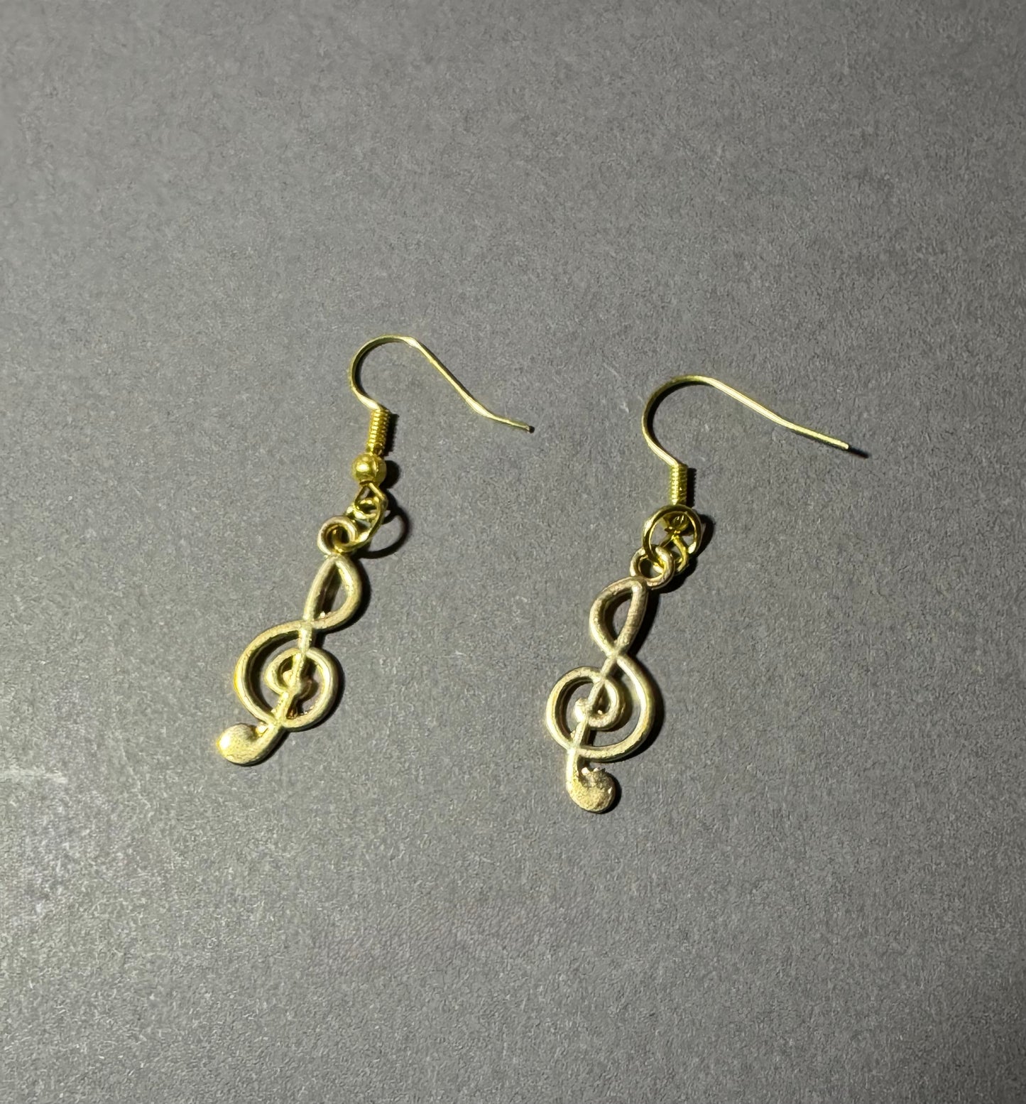 A pair of gold treble clef dangle earrings on a textured gray background.