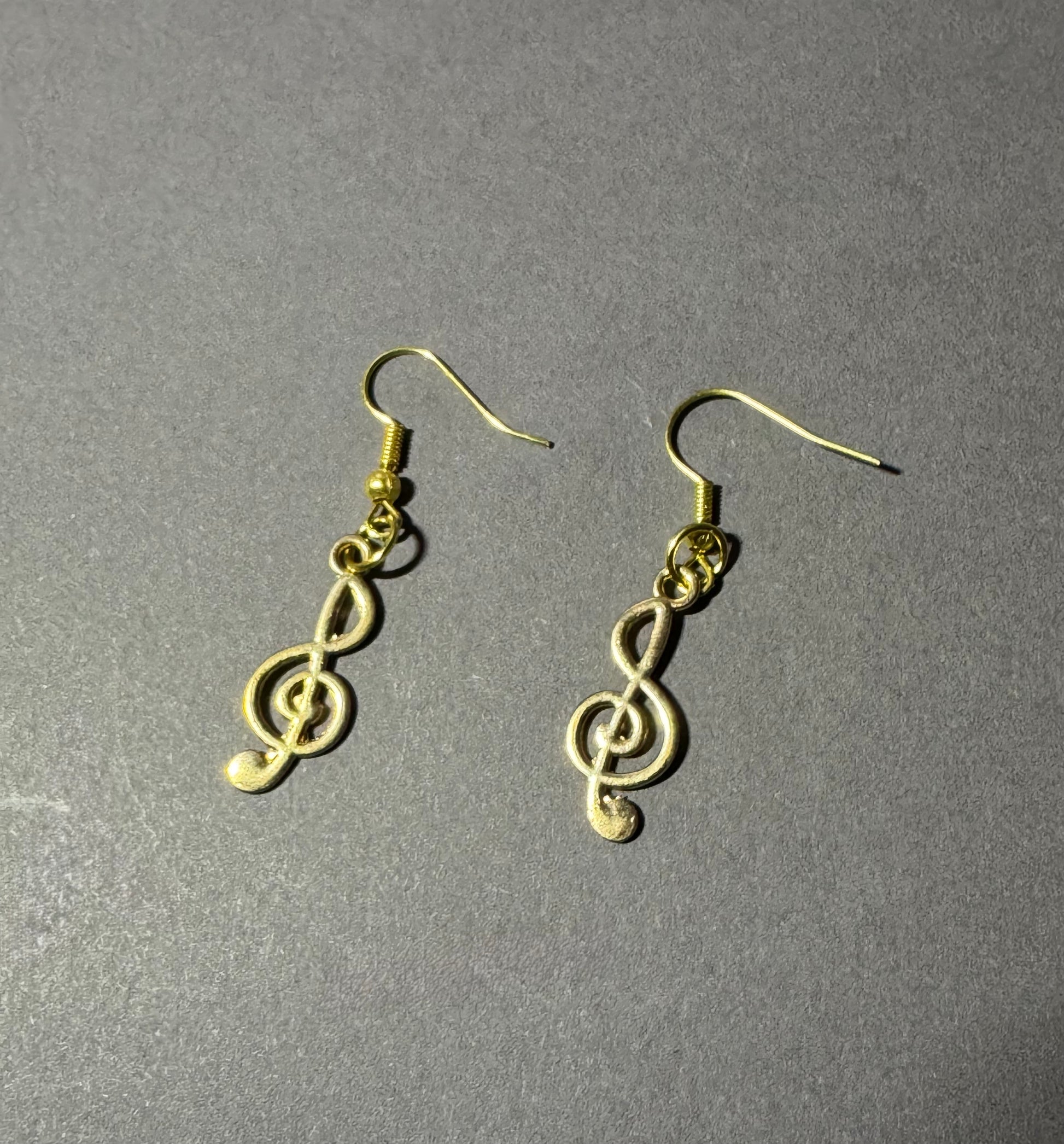 A pair of gold treble clef dangle earrings on a textured gray background.