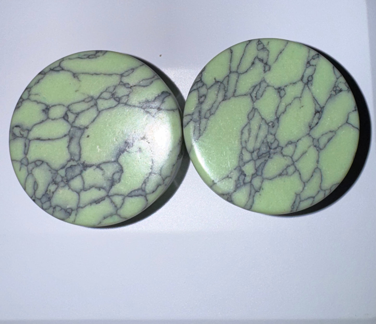 Two green marbled ear gauges on a white background