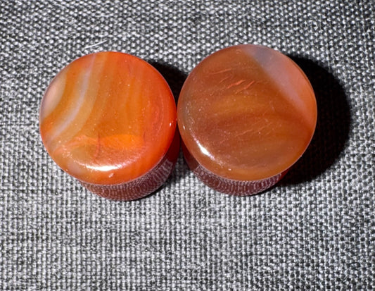 Two carnelian ear gauges on a textured gray background