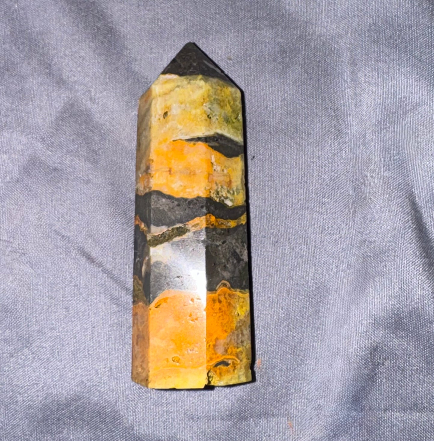 A natural quartz crystal point with layered bands of yellow, orange, black, and white, standing upright on a textured gray fabric background.